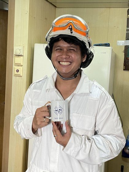 A crew member holding a Stella Maris welcome mug
