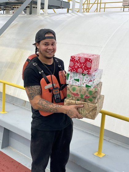 A crew member carrying a stack of wrapped Christmas gifts