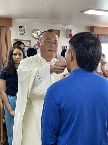 A priest giving communion to a crew member aboard ship