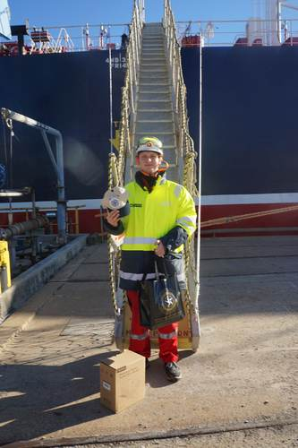 Crew member on a ship gangway holding a cap and welcome bag