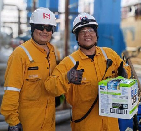 Two crew members in yellow coveralls giving a thumbs up while carrying a case of water at the Center.