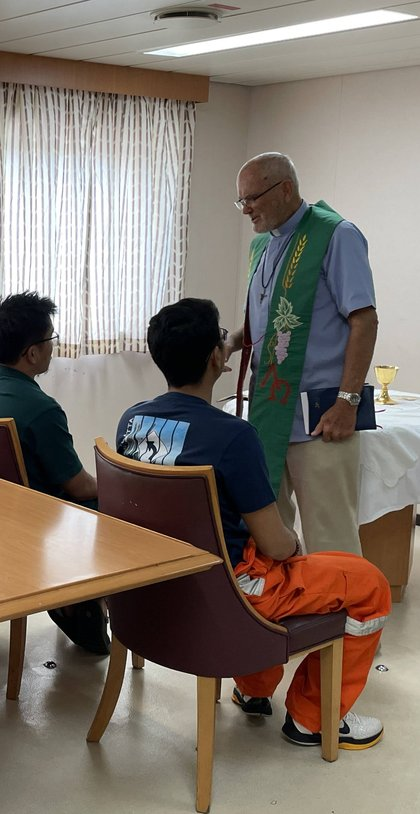 A priest speaking with crew members in the chapel