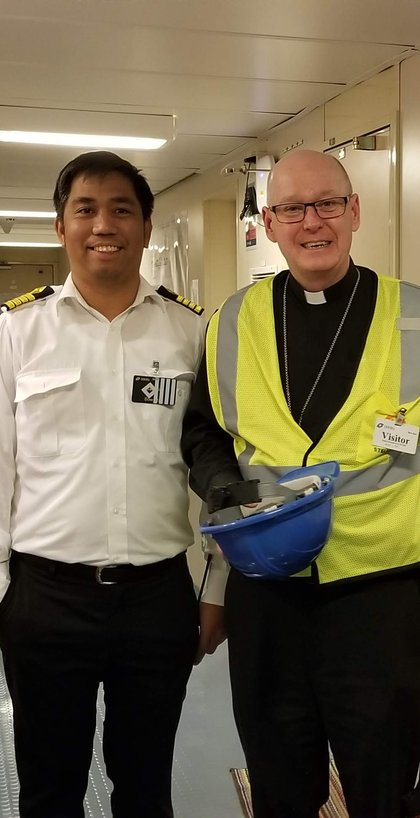 A ship officer and a visiting chaplain posing together aboard a vessel