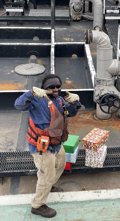 A crew member posing with wrapped Christmas gifts aboard a vessel