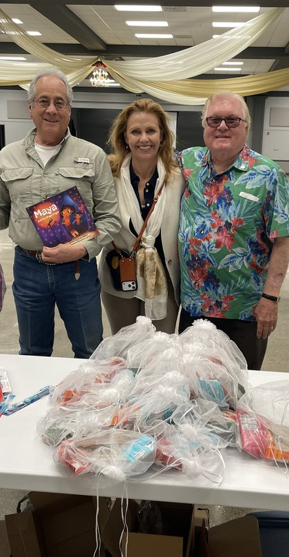 Friends posing with a children's book and gift bags at a fundraising event